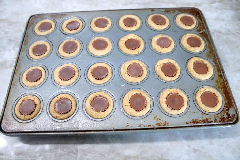Mini muffin pan filled with finished peanut butter cup cookies, each with a melted chocolate candy pressed into the center.