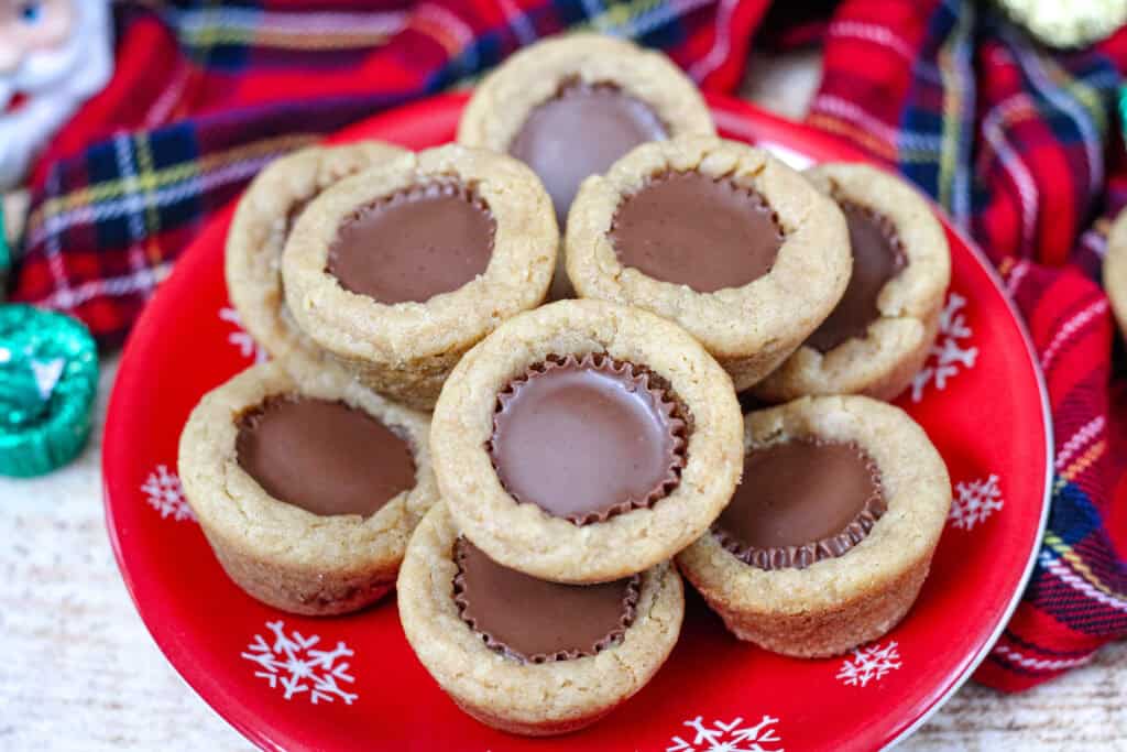 Close-up of soft peanut butter cup cookies arranged on a red snowflake plate, showing the melted chocolate centers.