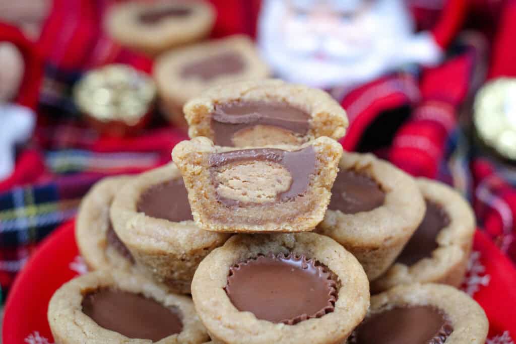 A peanut butter cup cookie sliced in half to reveal the soft peanut butter dough and chocolate center, displayed on top of a stack of cookies.