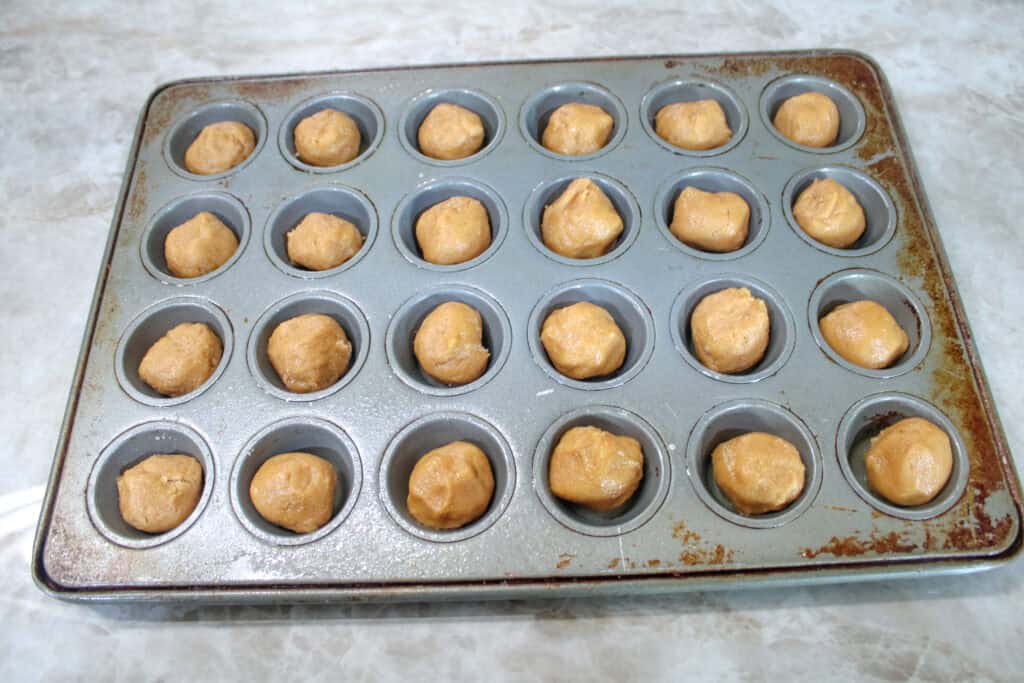 Mini muffin pan filled with rolled peanut butter cookie dough balls before baking.