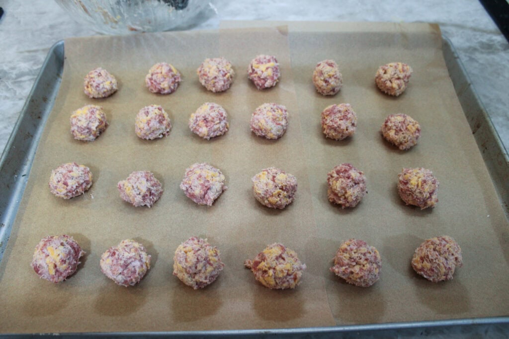 Unbaked sausage balls arranged on a parchment lined baking sheet before going into the oven.