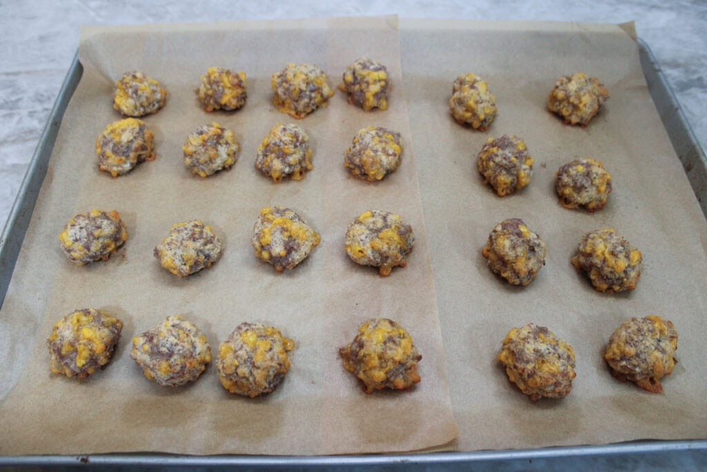 Baked sausage balls fresh from the oven, golden brown with melted cheddar cheese on parchment paper.