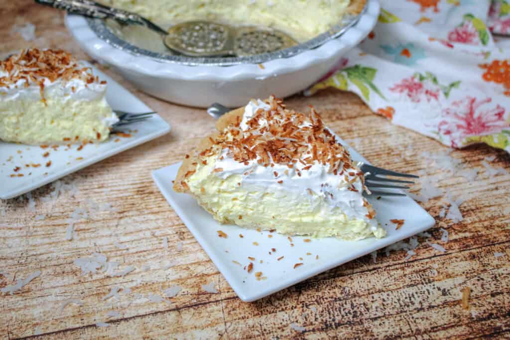 Slice of easy coconut cream pie topped with whipped topping and toasted coconut flakes on a white plate with fork.