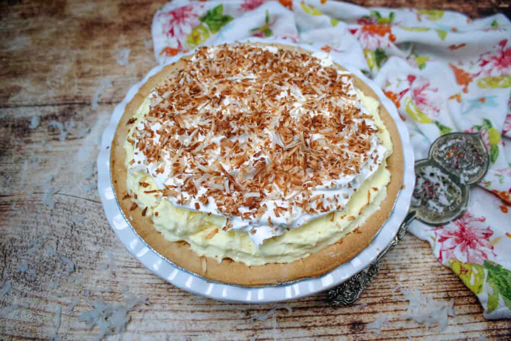 Whole easy coconut cream pie topped with whipped topping and toasted coconut in a baked pie crust on a white pie plate.