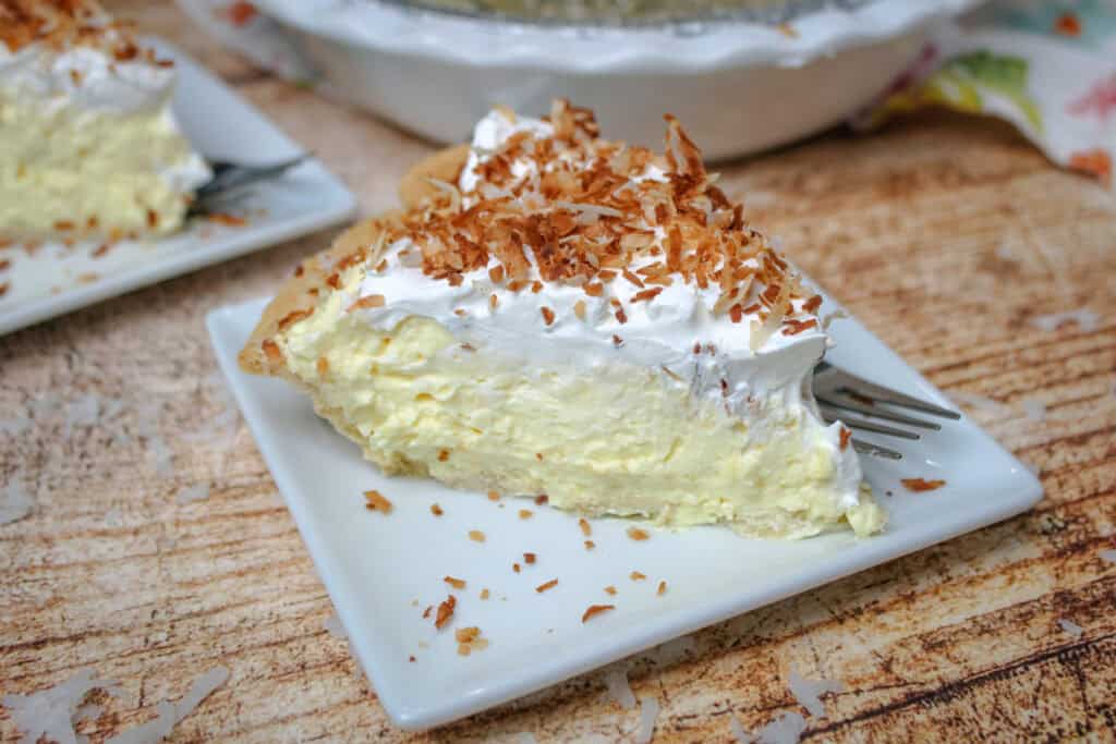 Close up slice of coconut cream pie showing thick creamy coconut filling, flaky crust, and toasted coconut topping.